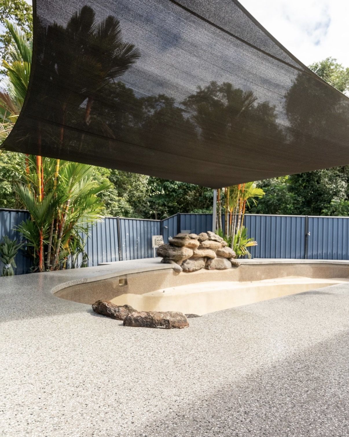 Exposed aggregate surround around a curved pool under a shade sail